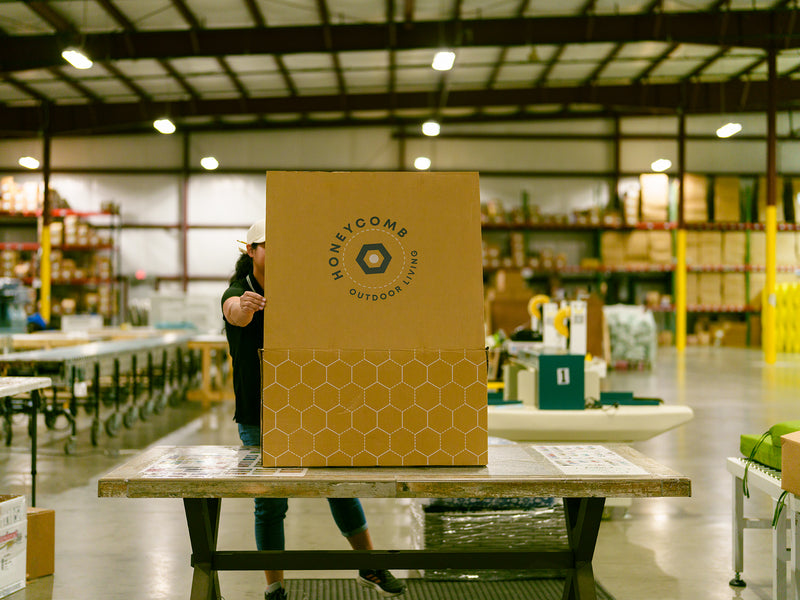 Image of the Honeycomb warehouse. A shipping box with the Honeycomb logo is in focus in the front, with the rest of the warehouse slightly blurred in the background.